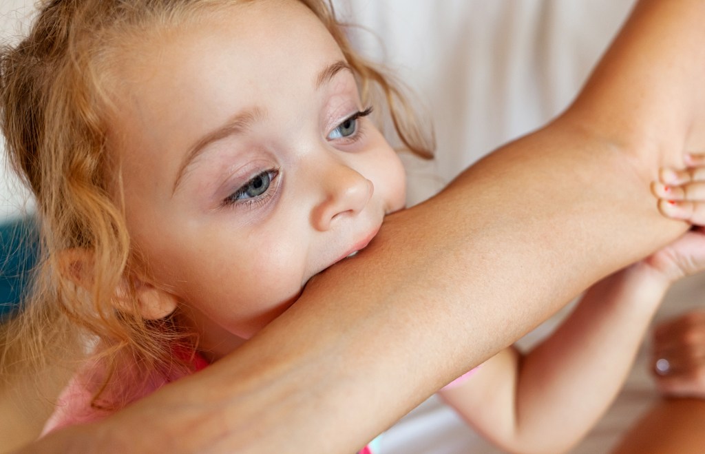 The mother is experiencing the biting phase of the little girl by biting her arm